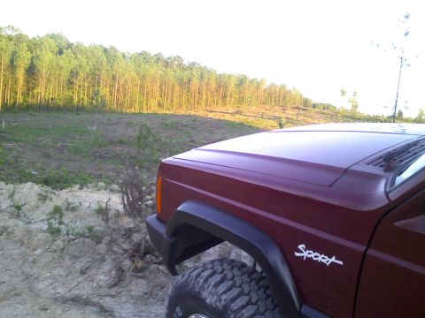 1998 Jeep Cherokee - A maroon Jeep Cherokee Sport is shown from the front quarter panel with a wooded area in the background.