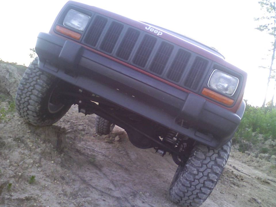 Red 1998 Jeep Cherokee flexing on a dirt hill with large tires