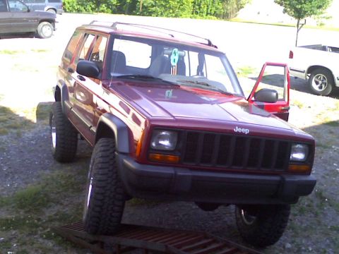 1998 Jeep Cherokee - Lifted 1998 Jeep Cherokee on a ramp with the driver's door open. Another vehicle is visible in the background.