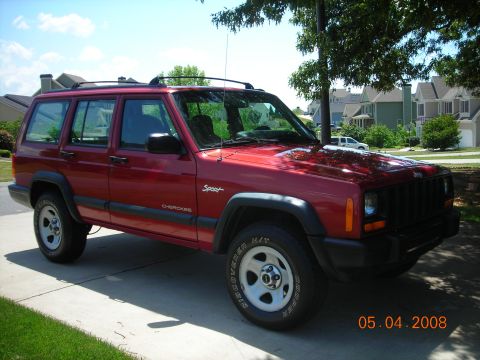 1998 Jeep Cherokee - This red Jeep Cherokee Sport SUV is parked on a driveway with houses in the background.