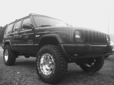 1998 Jeep Cherokee - A lifted 1998 Jeep Cherokee Sport sits on a gravel lot, ready for off-road adventures.