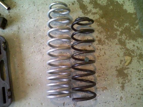 1998 Jeep Cherokee - Comparison of two coil springs, one silver and one black, laid out on a concrete surface.
