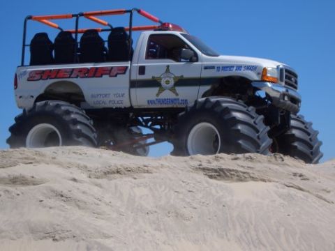 1991 Ford Crown Victoria - A modified truck with oversized tires and sheriff markings sits on a sandy dune under a clear blue sky.