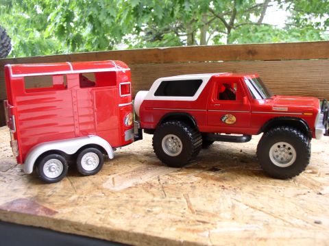 1979 Ford Bronco - A red toy 1978 Ford Bronco is shown towing a red toy trailer, both resting on a wooden surface.