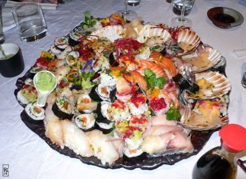 1991 Ford Crown Victoria - A large platter filled with various sushi rolls, sashimi, and seafood is presented on a table.