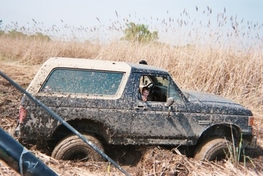 1990 Ford Bronco - A Ford Bronco is stuck in the mud, with a person visible in the driver's seat.