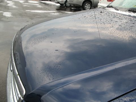 1971 Ford Ranchero - Water droplets dot the reflective surface of a dark blue car's hood, with other vehicles visible in the background.