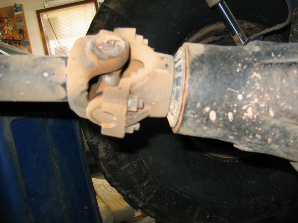 Close-up of a driveshaft U-joint connection to a differential housing, with a tire visible