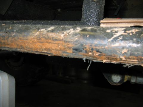 1992 Ford Mustang - The underside of a vehicle shows a heavily rusted frame rail with evidence of wear and tear.