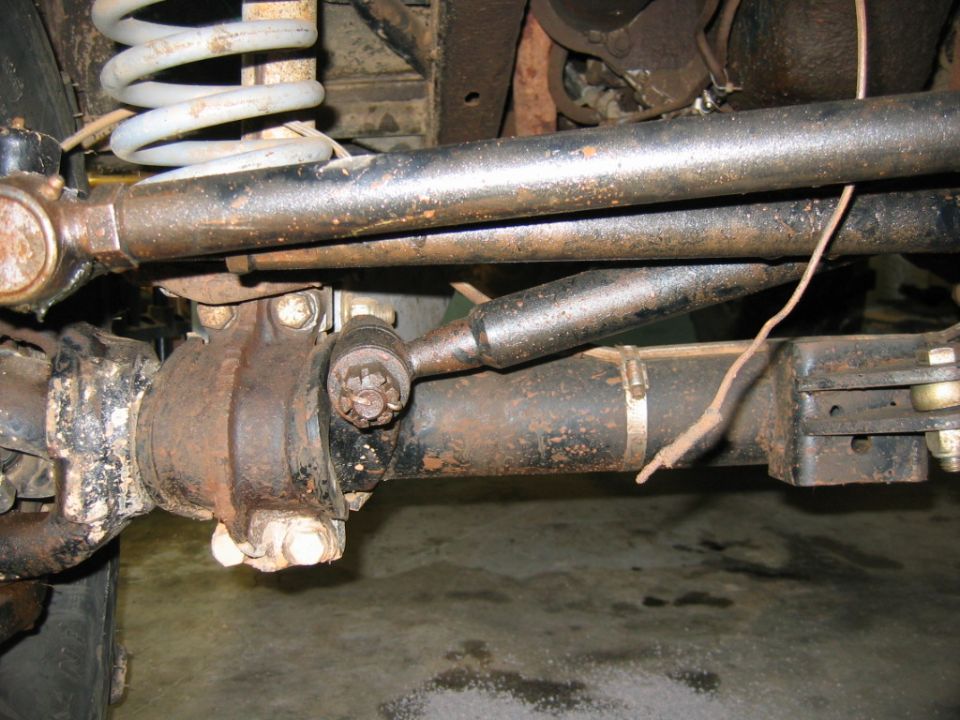 close-up of rusty steering linkage and coil spring on a vehicle's undercarriage