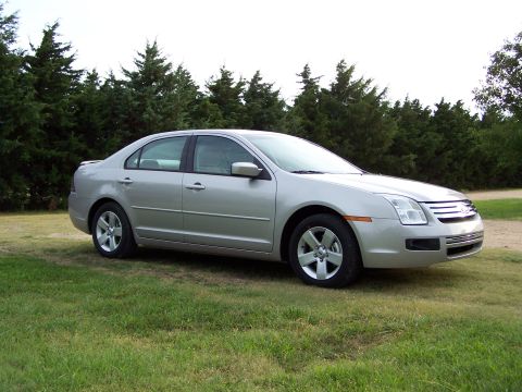 2008 Ford Fusion - Silver sedan parked on grass with trees in background. Grille indicates it is likely a 2006 model.