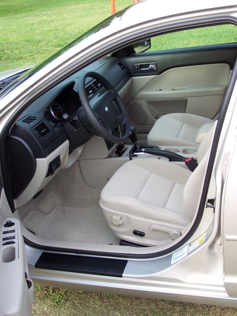 2008 Ford Fusion - The interior of a light-colored sedan, cloth seats and a black steering wheel, is viewed from the open passenger door.
