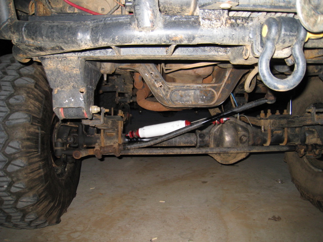 Underbody view of front solid axle steering linkage with white steering stabilizer and D-ring shackle