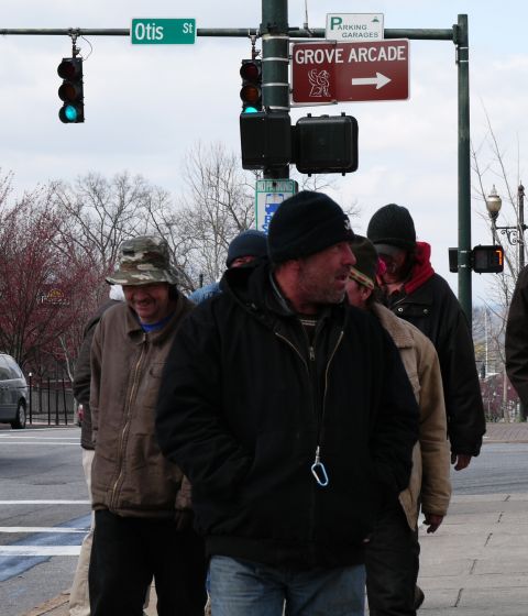 1985 Ford LTD Crown Victoria - A group of men walk along a city sidewalk near an intersection with street signs.