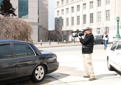 1985 Ford LTD Crown Victoria - A man films a dark gray Ford Crown Victoria parked on a city street next to a white car.