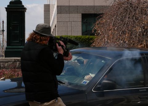 1985 Ford LTD Crown Victoria - A cameraman films a black sedan from which smoke is emerging.