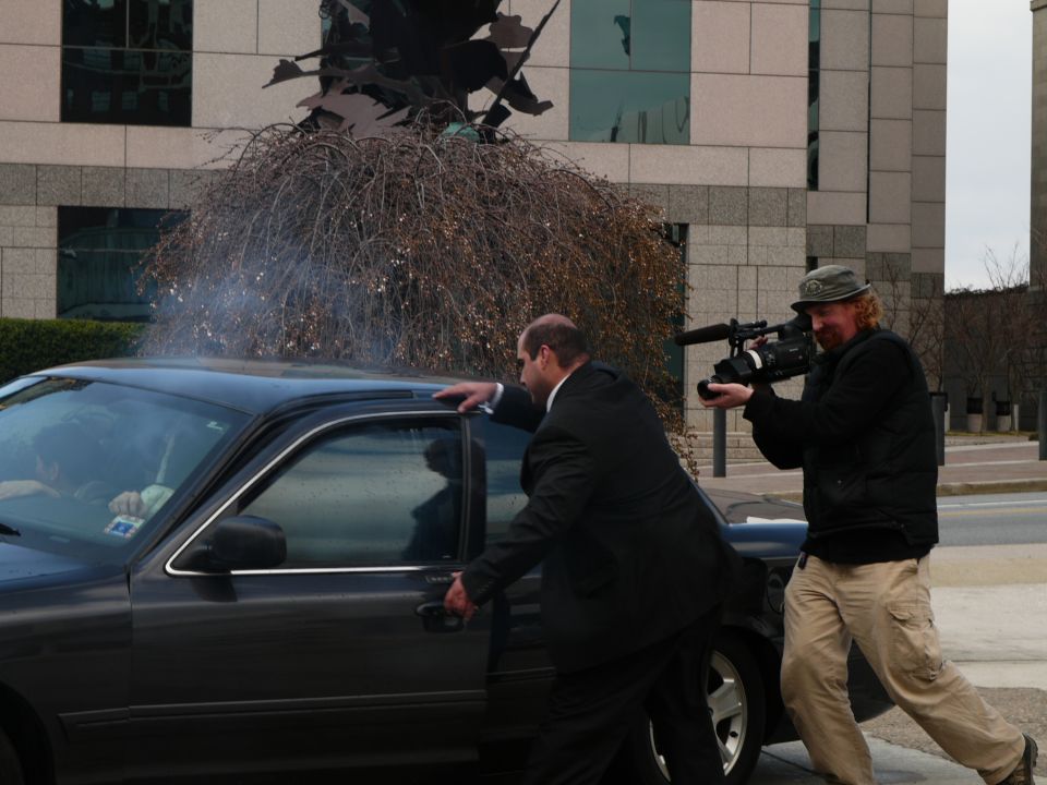 Dark sedan side view, man opening door, cameraman filming