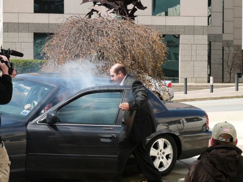1985 Ford LTD Crown Victoria - Man exits car as smoke billows from the open door. Another vehicle is visible in the background.