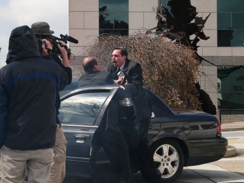 1985 Ford LTD Crown Victoria - A film crew captures a dramatic scene where two men in suits appear to be arguing next to a car.