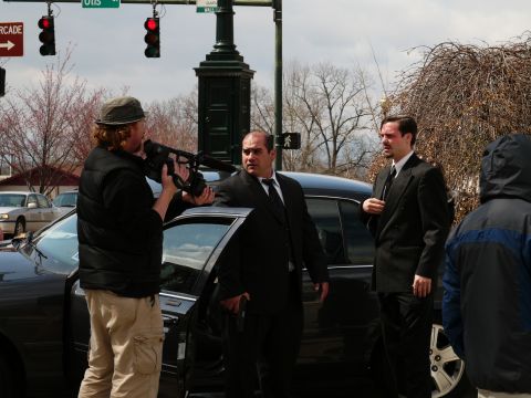1985 Ford LTD Crown Victoria - A black sedan is parked on a street with three men in suits around it, one holding a camera.