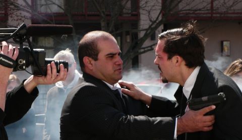 1985 Ford LTD Crown Victoria - A dramatic scene unfolds as two men confront each other, one holding a gun, while a camera operator films the event.