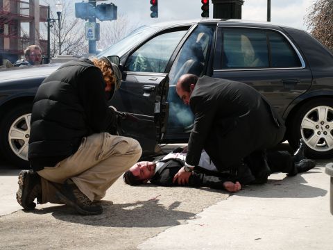 1985 Ford LTD Crown Victoria - Two individuals tend to a man lying on the ground next to a dark sedan.