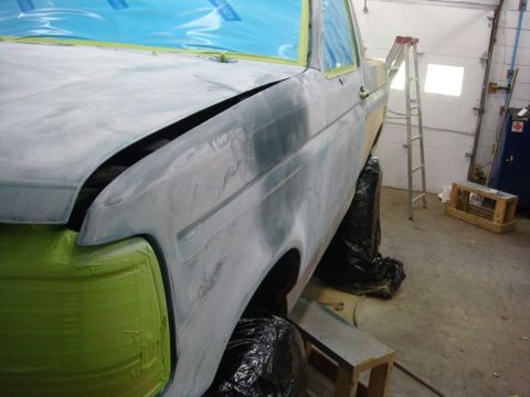 1996 Ford Bronco - A truck is being prepped for body repair, covered in primer and tape in a garage setting.
