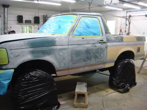 1996 Ford Bronco - A truck body is being prepped for paint, with windows covered and the body in primer.