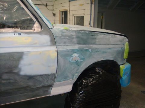 1996 Ford Bronco - Side view of a 1996 Ford Bronco undergoing body repair, showing primer and filler on the fender and door.