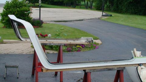 1979 Ford Bronco - White car door frame, likely for a classic vehicle, is disassembled and resting on sawhorses outdoors.