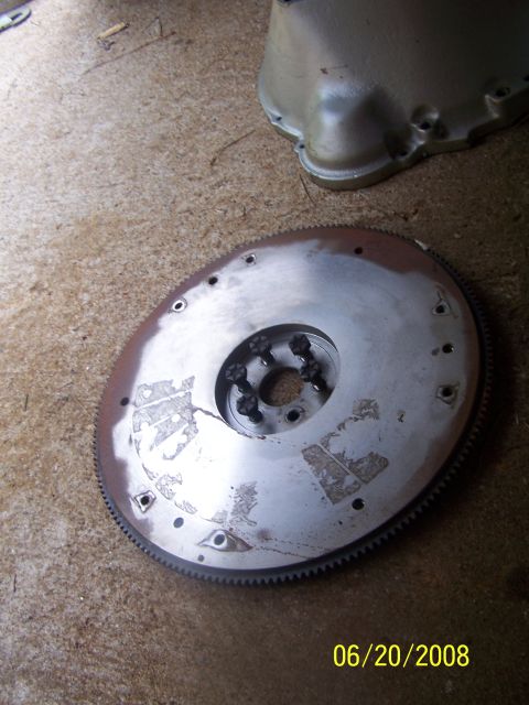 1979 Ford F-150 - A metal flywheel with a toothed edge and bolted central hub sits on a concrete floor next to a transmission casing.