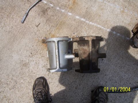 1979 Ford F-150 - Two engine components are laid out on a concrete surface, with a tool and footwear visible.