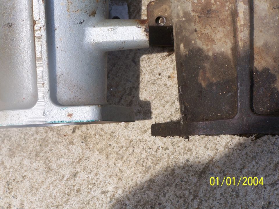 Two metal parts, one light gray and one rusty brown, sit on a textured surface. A date stamp reads 01/01/2004