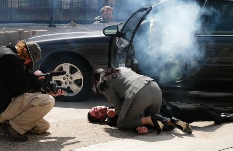1985 Ford LTD Crown Victoria - A film crew captures a dramatic scene involving a black sedan, smoke, and actors on the ground.