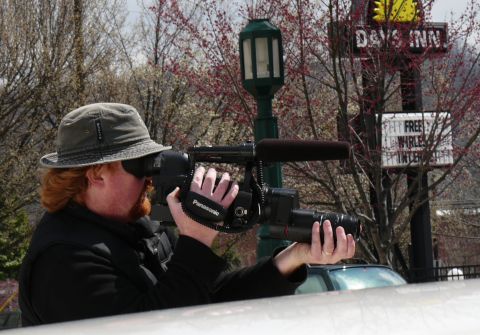 1985 Ford LTD Crown Victoria - A man films with a camcorder, with a white car and a Days Inn sign visible in the background.
