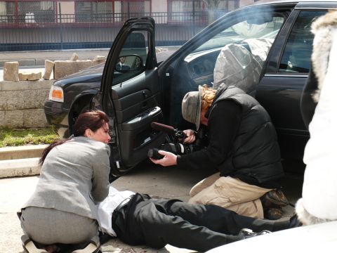 1985 Ford LTD Crown Victoria - A film crew captures a dramatic scene involving a person on the ground and a car.