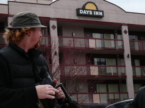 1985 Ford LTD Crown Victoria - A man holding a rifle stands in front of a Days Inn hotel.