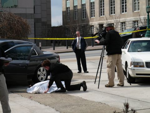 1985 Ford LTD Crown Victoria - A crime scene unfolds with a covered body, two vehicles, a cameraman filming, and police tape cordoning off the area.