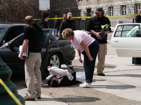 1985 Ford LTD Crown Victoria - Investigators examine a scene where a person is lying on the ground near a black car.