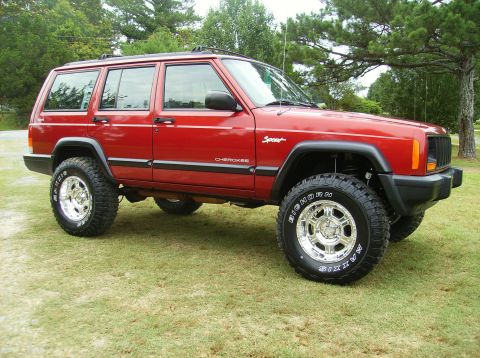 1998 Jeep Cherokee - This red 1998 Jeep Cherokee Sport features aftermarket wheels and tires, parked outdoors on a grassy lawn.
