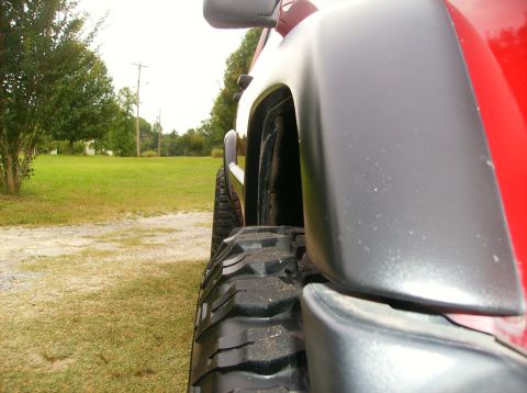 1998 Jeep Cherokee - Close-up side view of a red SUV's fender and off-road tire, consistent with a 1998 Jeep Cherokee.