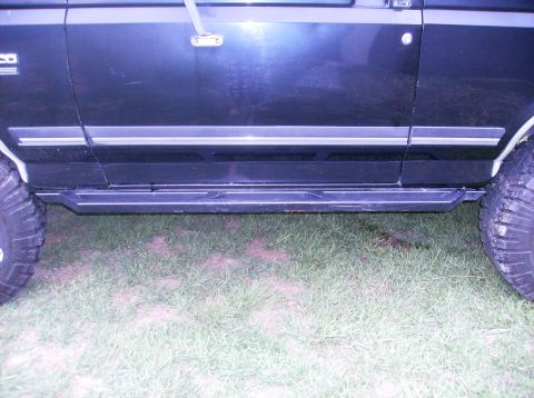 1990 Ford Bronco - The side view of a dark colored SUV shows a step bar installed below the doors. The vehicle is parked on a grassy area.
