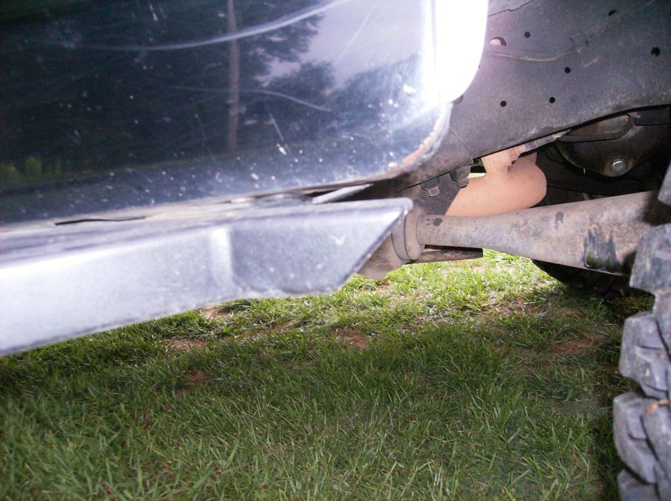 Undercarriage of a dark vehicle showing frame, suspension, and exhaust pipe on grass.