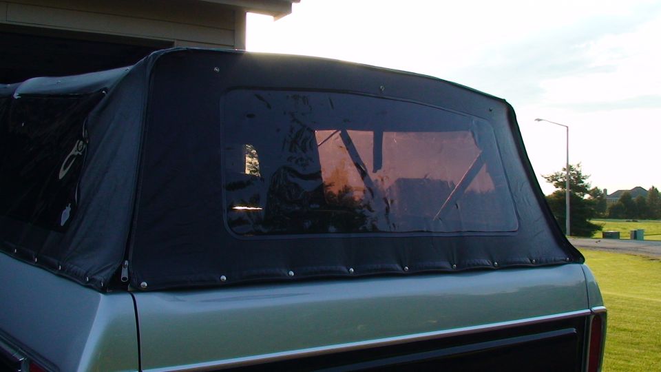 Rear view of a pickup truck with a black soft top and clear window.