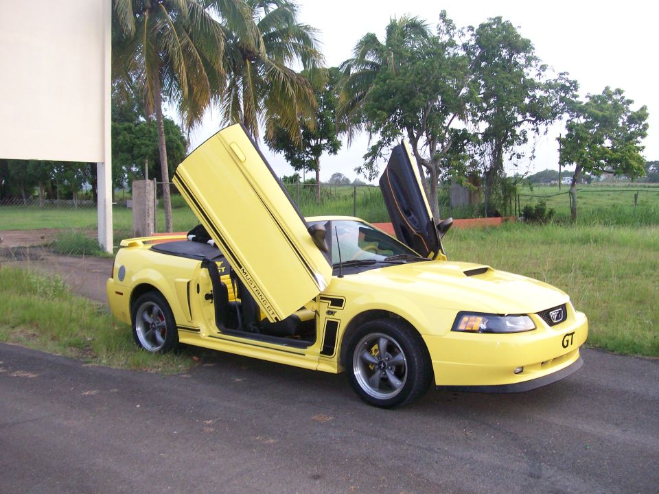 Yellow 2001 Ford Mustang convertible with doors open, parked on a road.