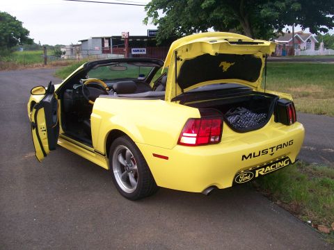 2001 Ford Mustang - A bright yellow 2001 Ford Mustang convertible is parked on a paved road with its driver's side door and trunk open. The car has a black int…