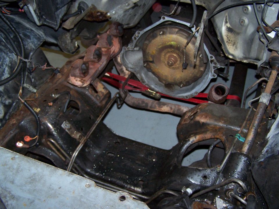 1985 Ford Bronco engine bay with rusted transmission, exhaust manifolds, and frame