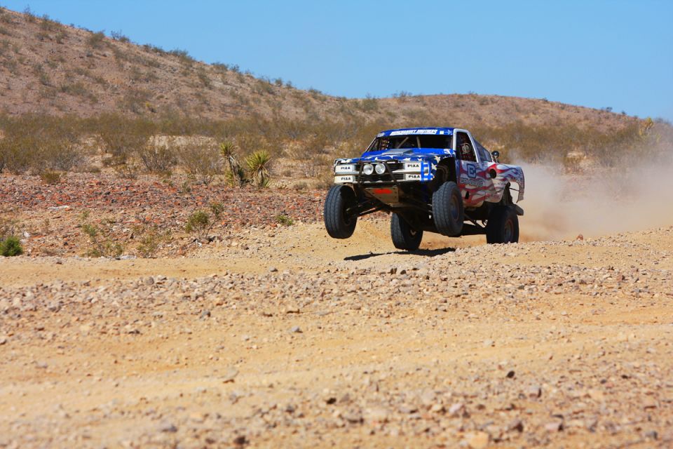 Off-road racing truck jumping over a dirt track in a desert.