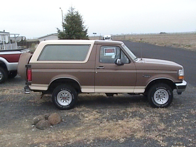 Side view of a brown and tan Ford Bronco with a "For Sale" sign in the window.