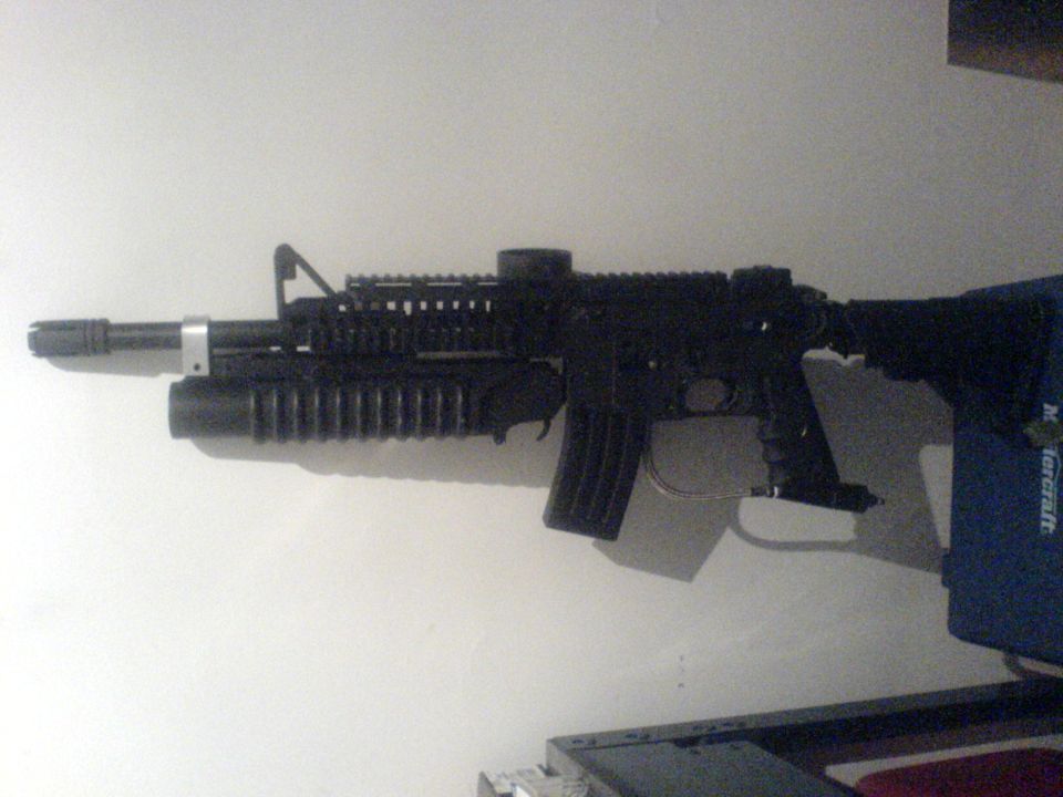 Black airsoft rifle with grenade launcher attachment on a white wall.